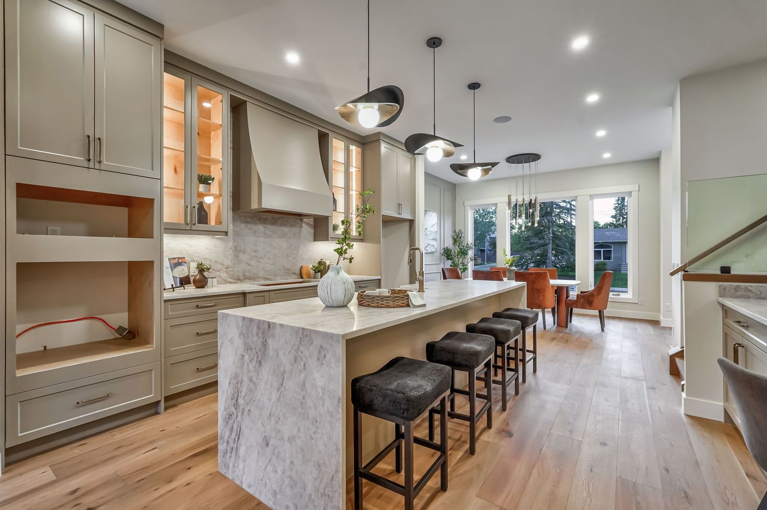Modern kitchen with marble island, gray cabinets, pendant lights, and bar stools on light hardwood floors.