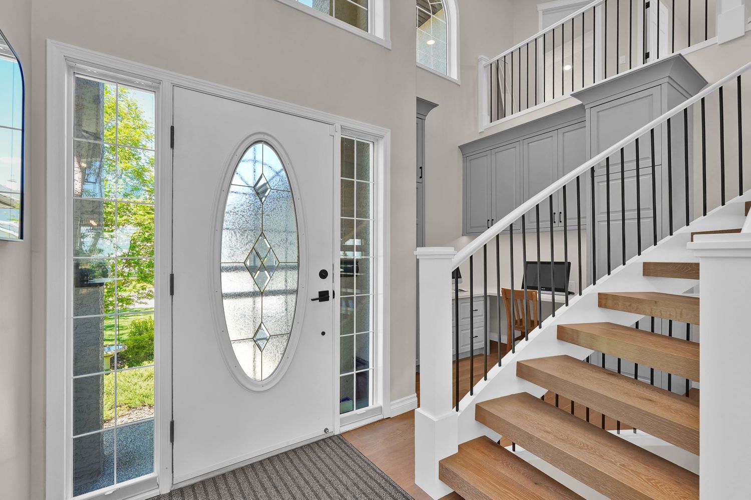 Bright foyer with white front door featuring oval glass insert, sidelights, and elegant staircase with wood steps.