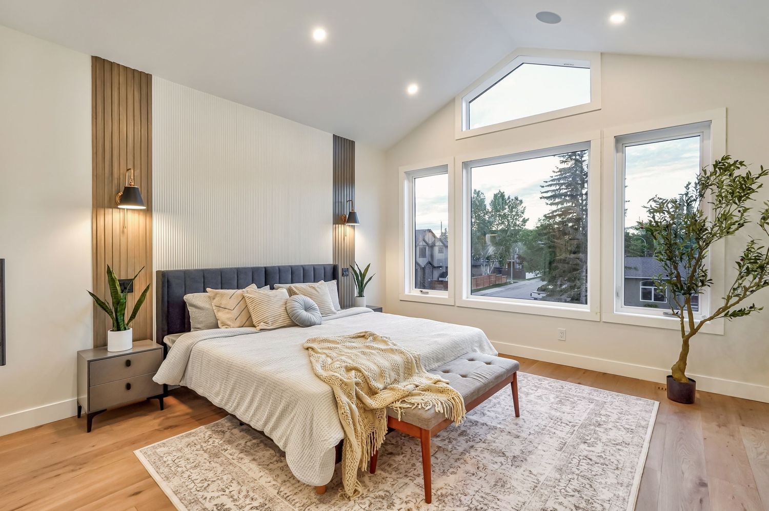 Bright modern bedroom with vaulted ceiling, large windows, hardwood floors, and elegant neutral decor.