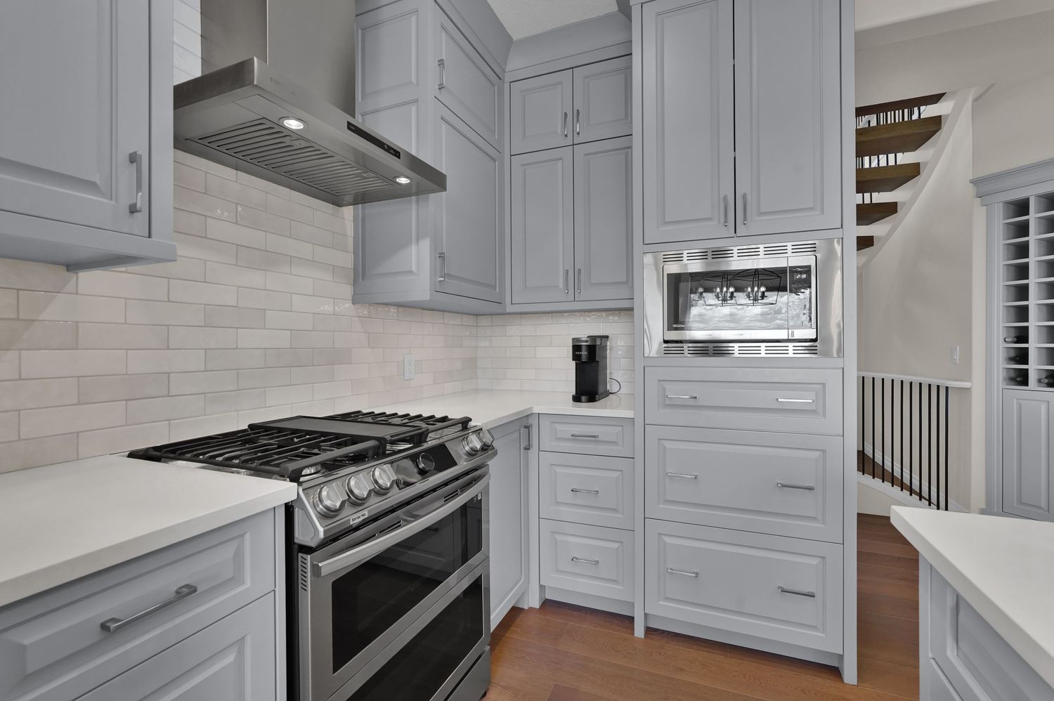 Gray shaker kitchen cabinets with marble backsplash, stainless steel range, and vent hood in modern kitchen.