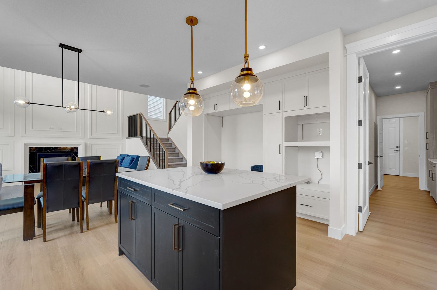 Open-concept kitchen with dark island, gold pendant lights, white cabinetry, and hardwood floors.