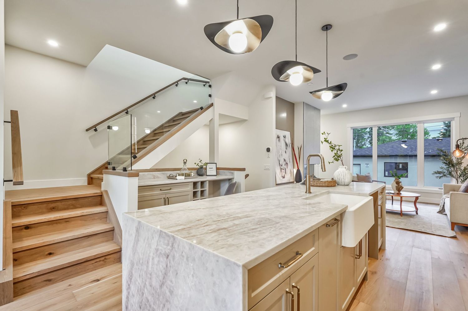 Modern kitchen island with marble countertop, pendant lights, and open staircase in a bright, contemporary home.