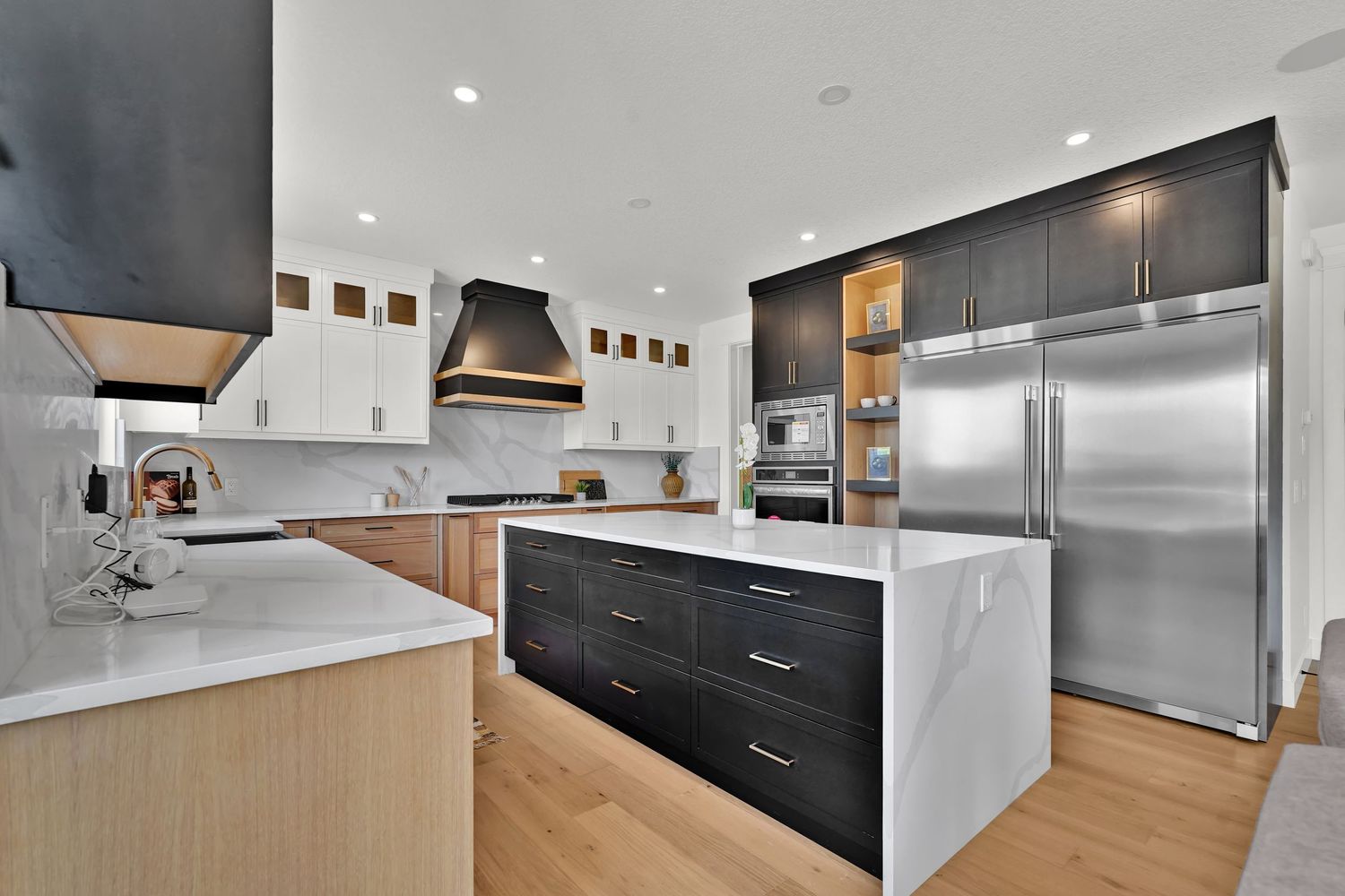 Modern kitchen with dark lower cabinets, white uppers, marble island, and stainless steel appliances.