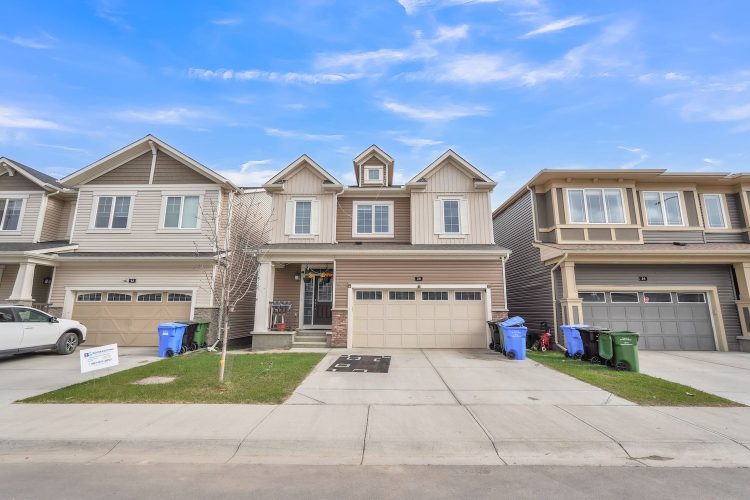 Modern townhome exterior with tan siding, double garage, decorative brick, and well-kept front yard.