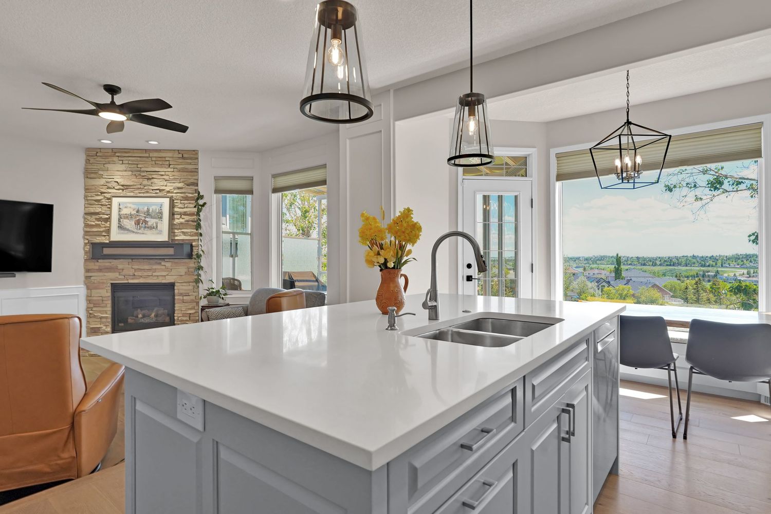 Modern kitchen island with white quartz countertop, gray cabinets, and pendant lights overlooking a scenic outdoor view.