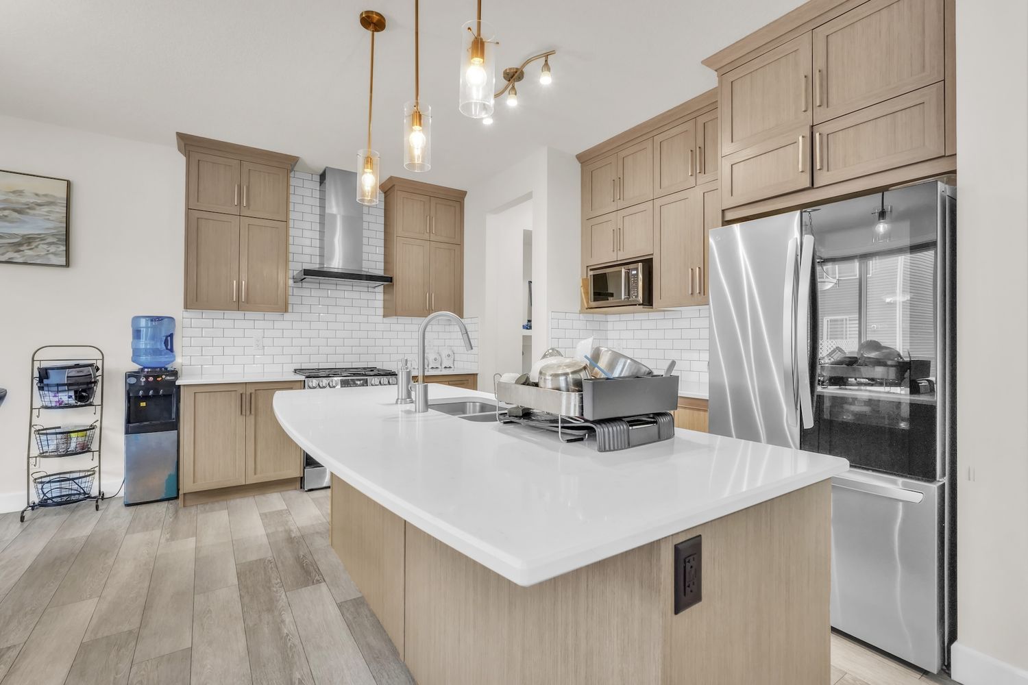 Contemporary kitchen featuring tan cabinets, white quartz countertop island, stainless appliances, and stylish pendants.