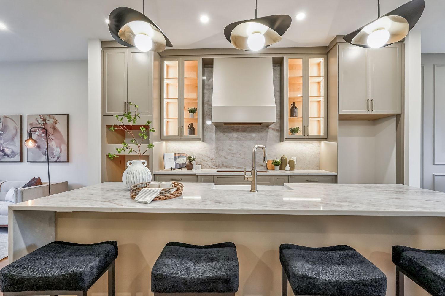 Modern kitchen with quartz island, black barstools, pendant lights, glass cabinets, and custom range hood.