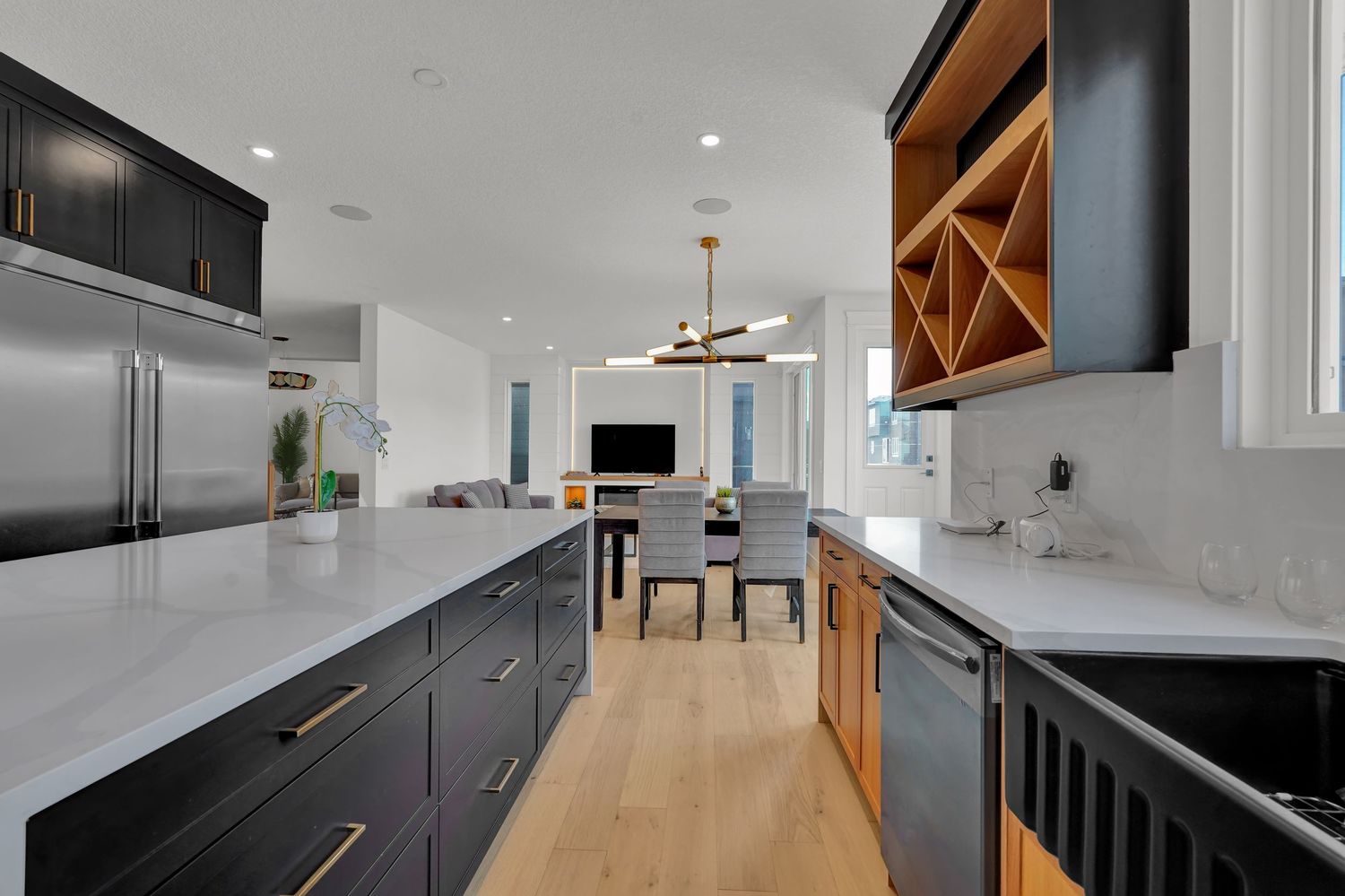 Sleek kitchen featuring dark cabinets, white quartz countertops, wood wine rack, and stainless steel appliances.