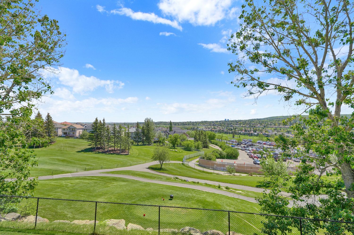 Scenic view of lush green golf course with trees, blue sky, and residential neighborhood in the background on a sunny day.
