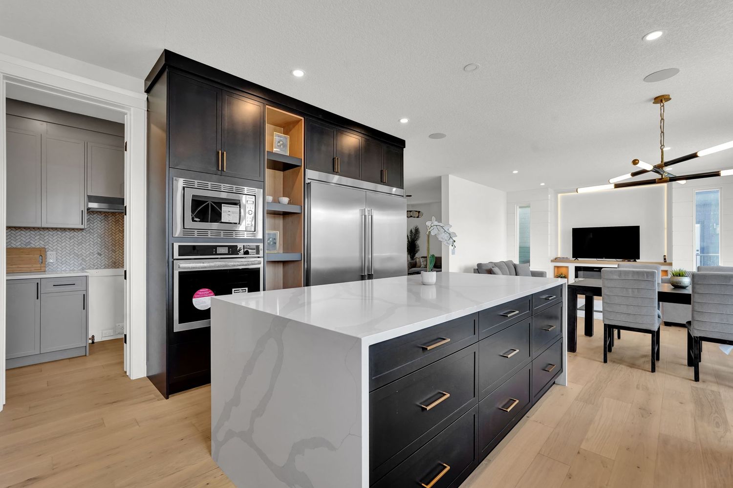 Modern kitchen with dark cabinetry, white quartz island, stainless steel appliances, and gold hardware accents.