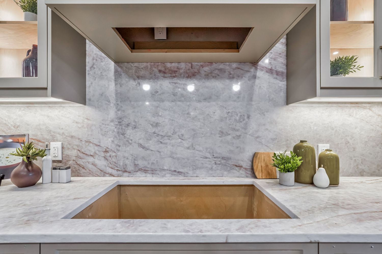 Elegant kitchen featuring a marble backsplash, undermount sink, white quartz countertops, and gray cabinetry with warm lighting.