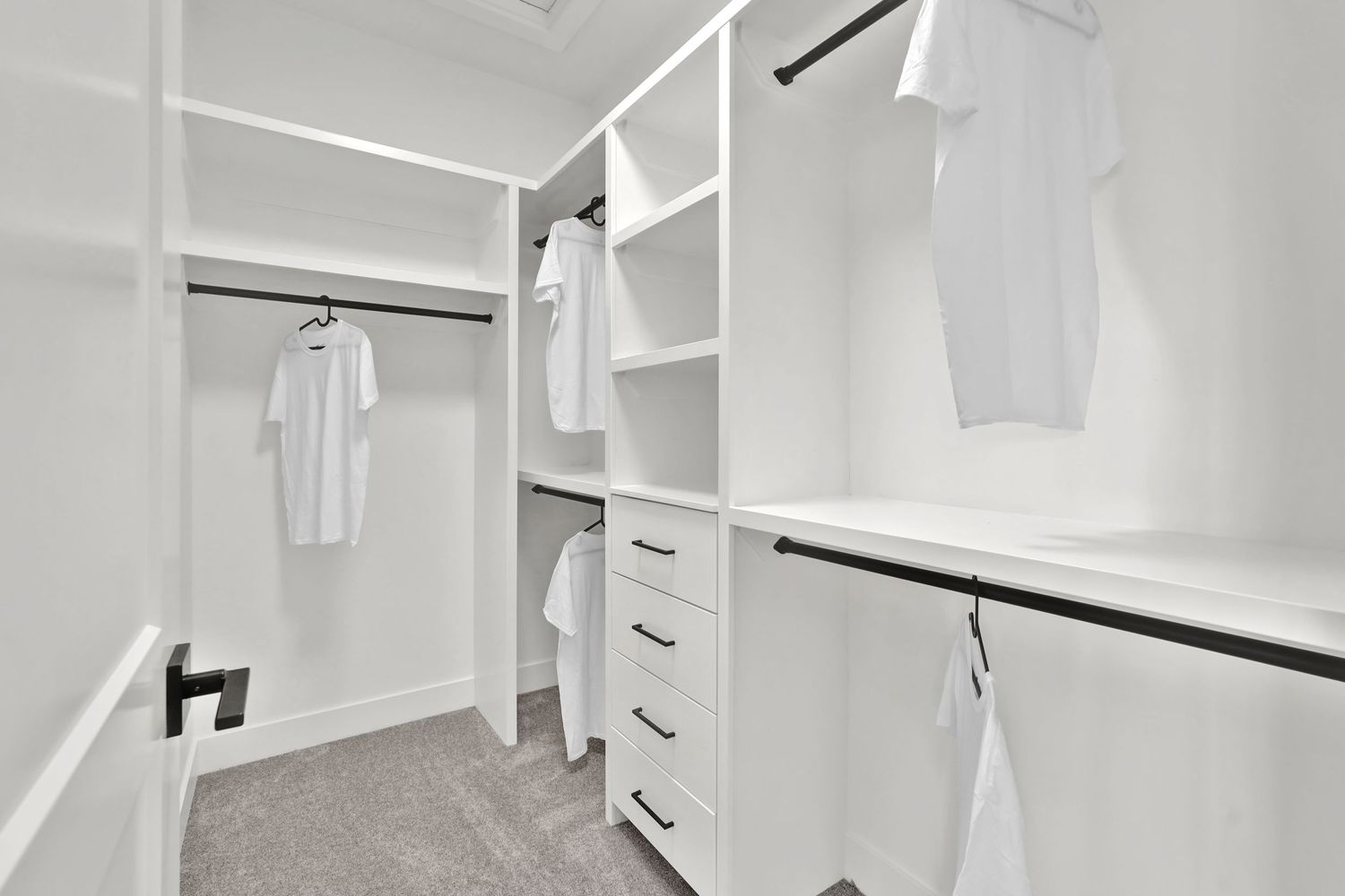 Spacious walk-in closet with white built-in shelving, drawers, and hanging rods with white shirts displayed.