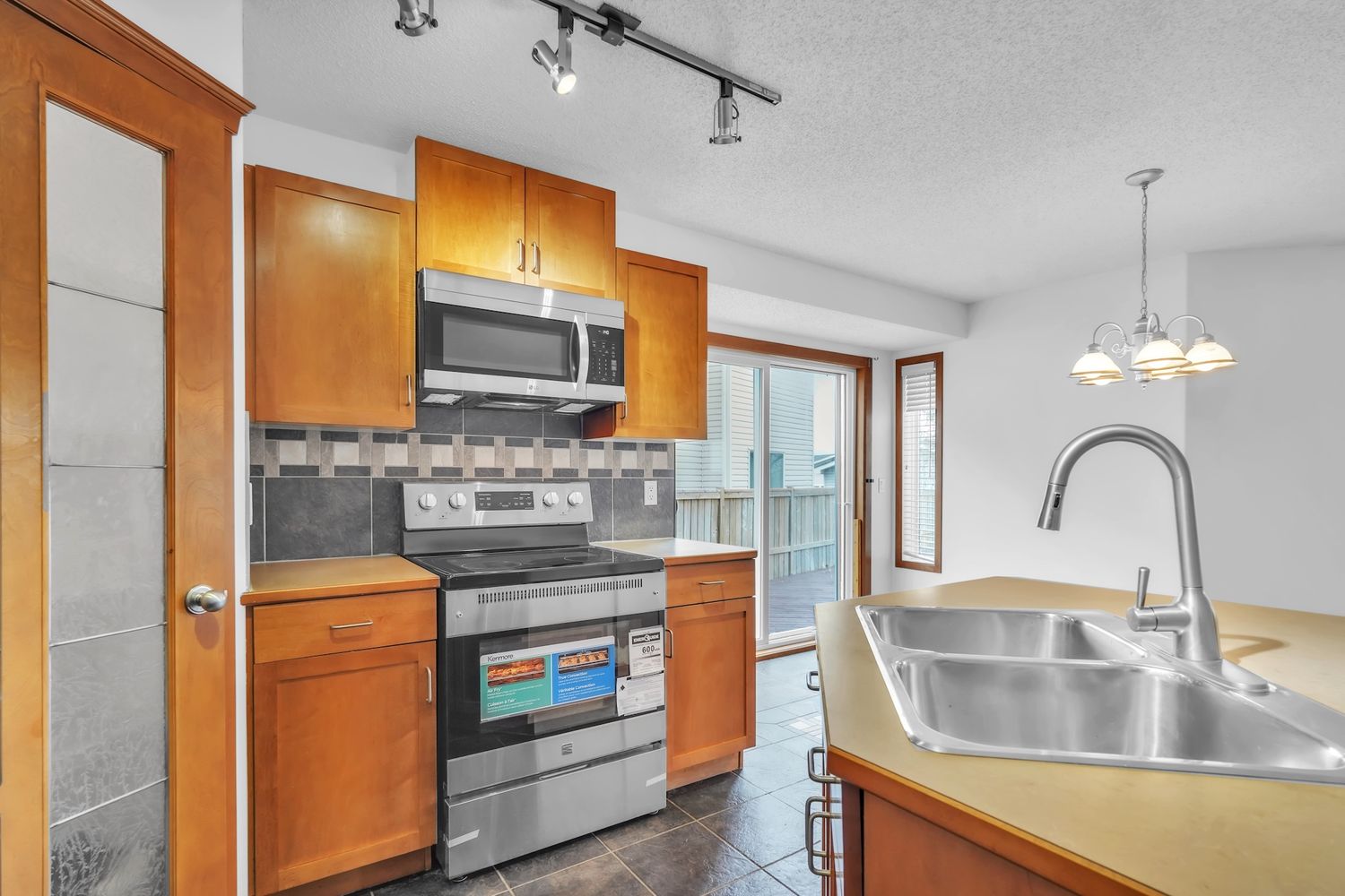 Compact kitchen with honey oak cabinets, stainless steel appliances, tile backsplash, and double sink.