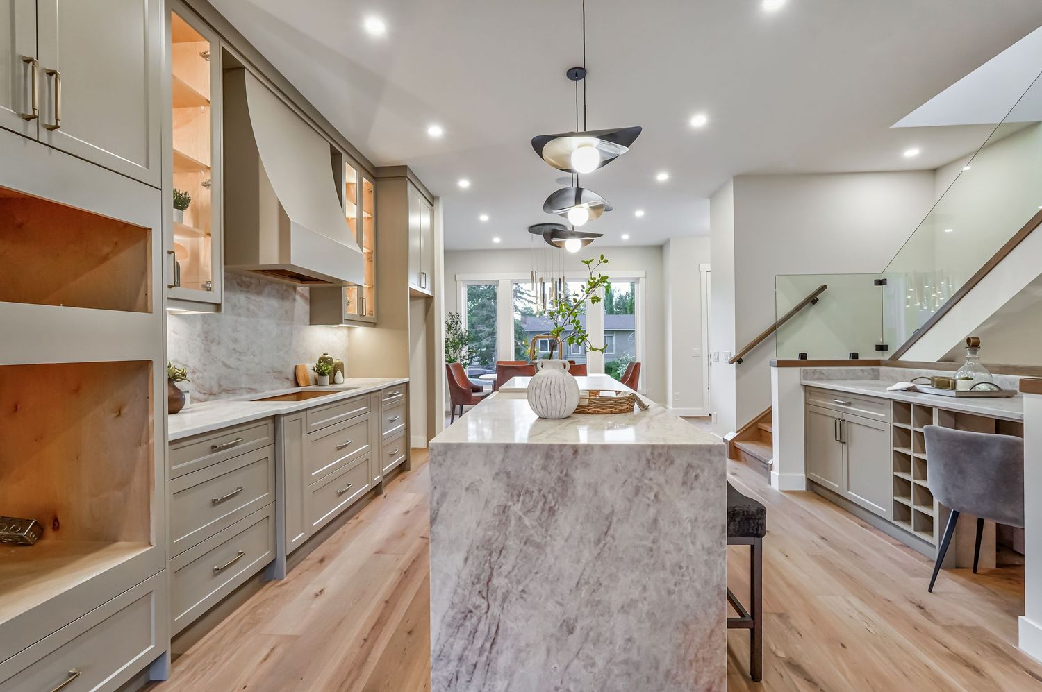 Modern open-concept kitchen with marble island, sage cabinets, hardwood floors, and view into bright living area with staircase.