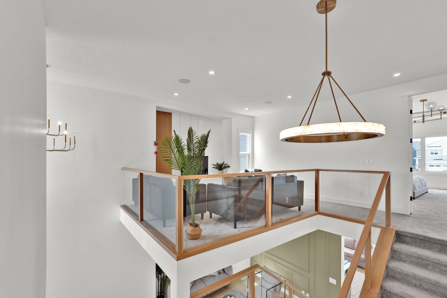 Bright open loft area with glass railing, wood staircase, circular pendant light, and recessed lighting.
