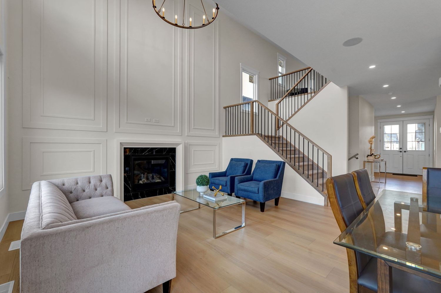 Bright living room with high ceilings, fireplace, blue accent chairs, staircase, and hardwood floors.