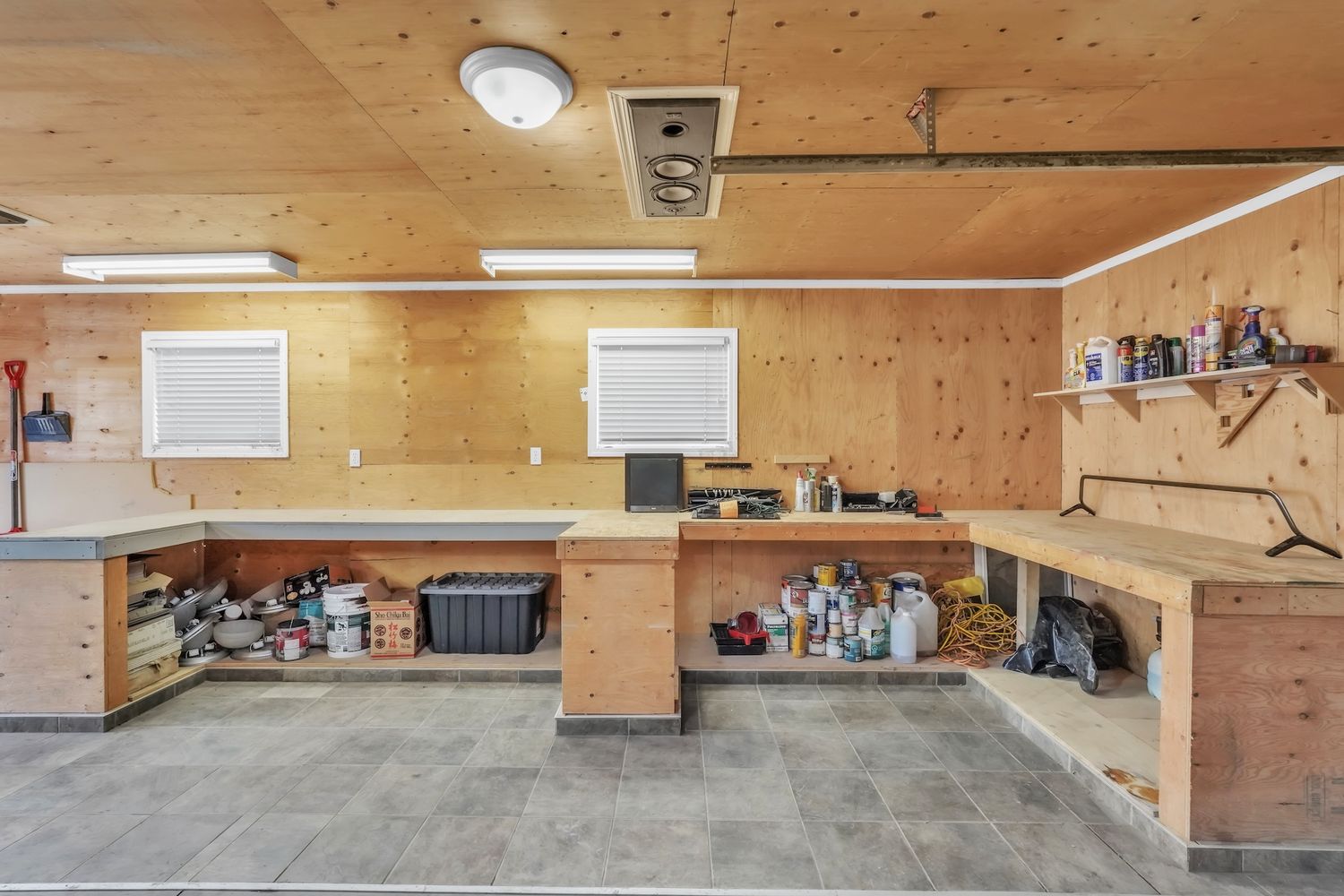 Spacious workshop garage interior with built-in wood workbenches, shelving, and overhead fluorescent lighting.