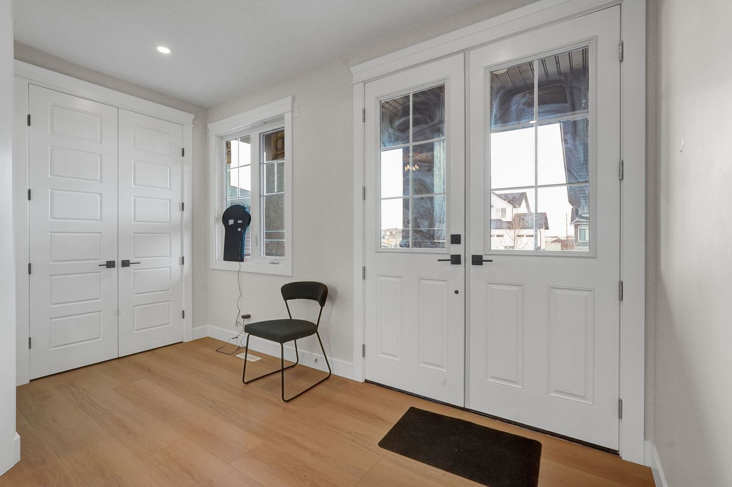 Bright entryway with white double doors, sidelights, hardwood floors, and closet storage.