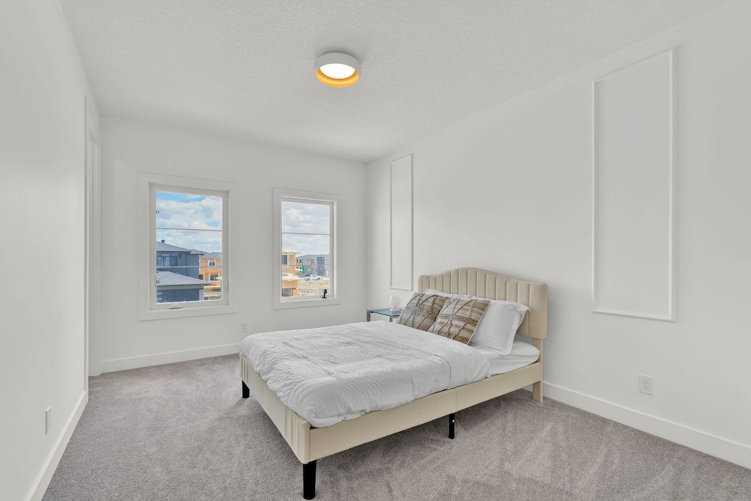 Minimalist bedroom with beige carpet, upholstered headboard, neutral walls, and two large windows.