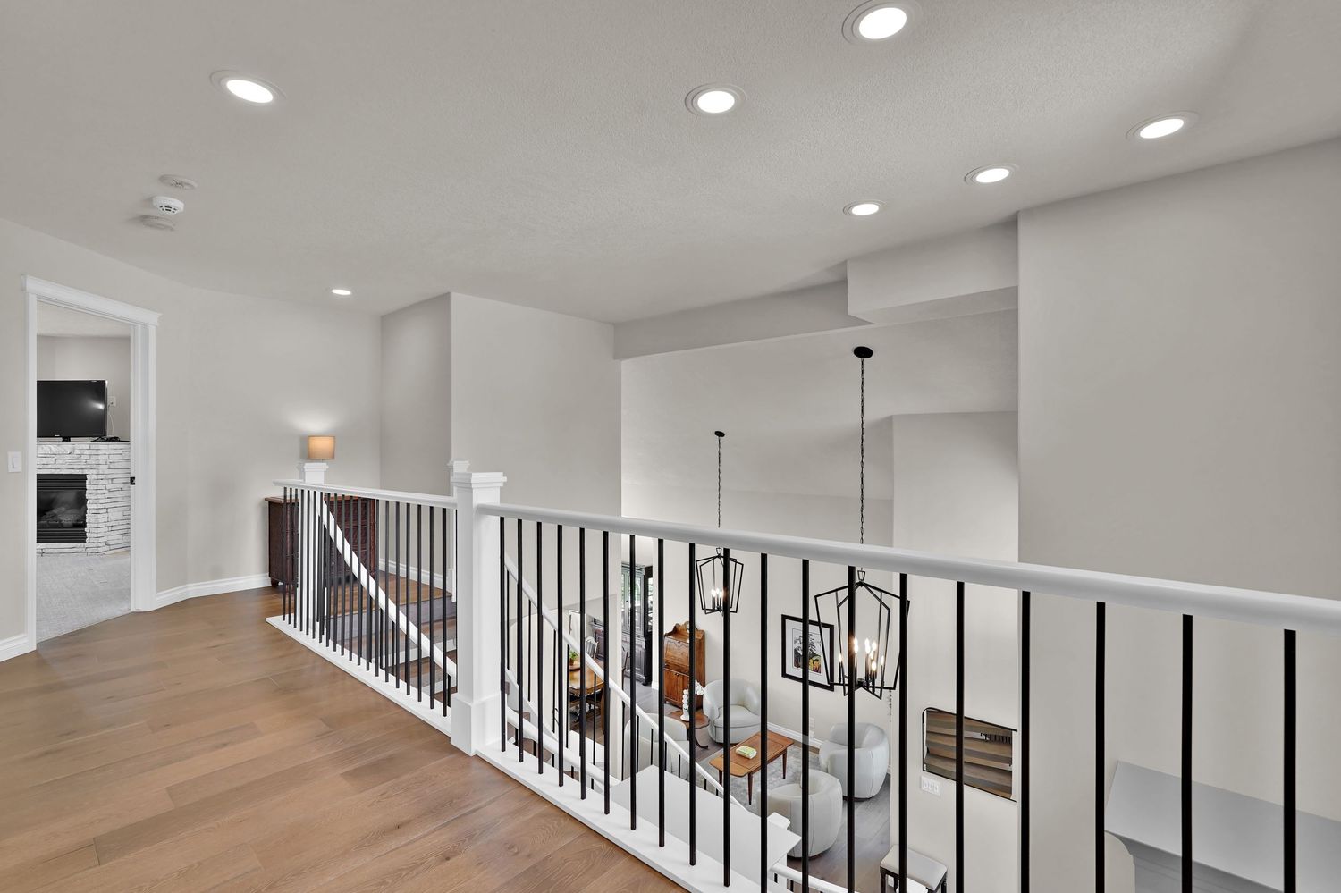 Modern hallway with hardwood floors, white walls, recessed lighting, and black metal stair railing in a luxury home.