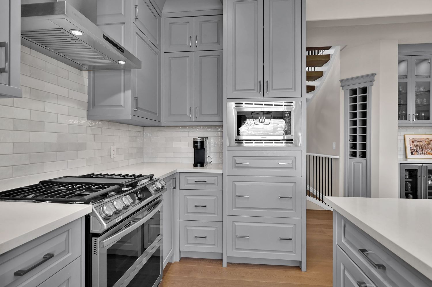 Modern kitchen with gray shaker cabinets, subway tile backsplash, stainless steel range, and built-in microwave on hardwood floors.