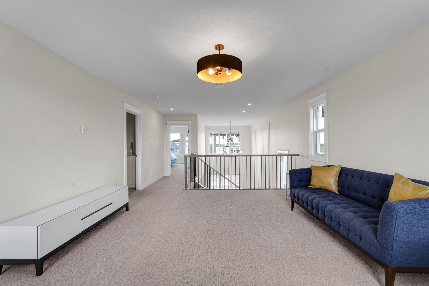 Carpeted upper-floor bonus room with blue velvet sofa, open railing, and natural light.