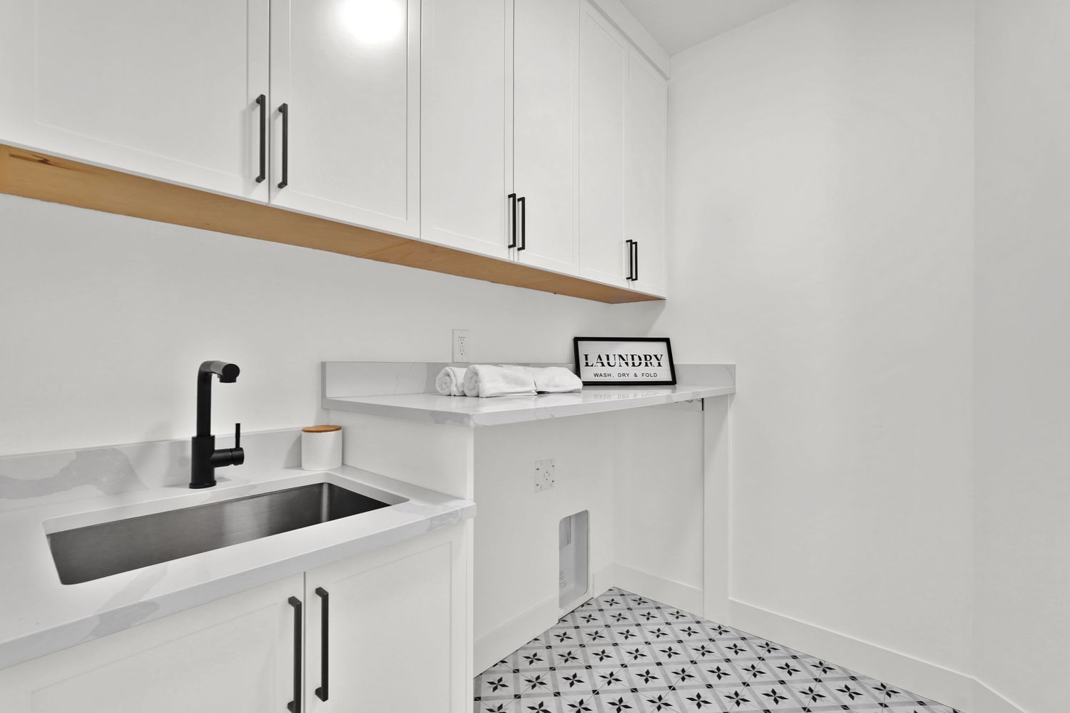 Modern white laundry room with marble countertop, undermount sink, black fixtures, and patterned tile floor.