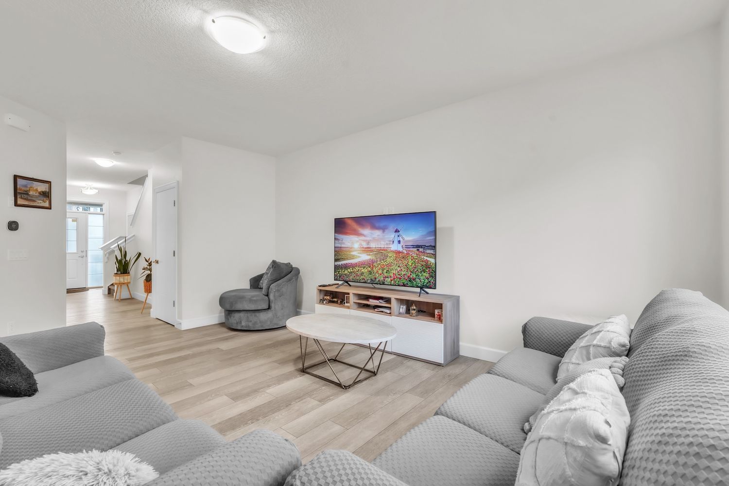 Spacious bright living room with gray sectional sofa, large TV, and light hardwood floors.