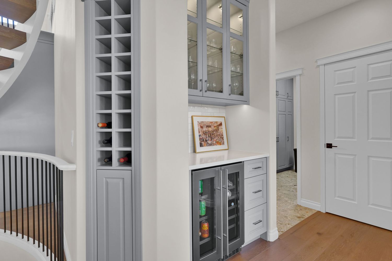 Gray built-in wine rack and glass-front cabinets with beverage fridge in elegant white home bar area.