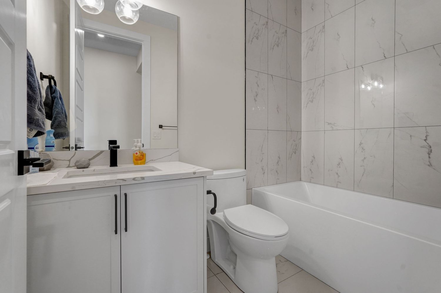 Clean white bathroom with marble-tiled tub surround, vanity, and modern black fixtures.