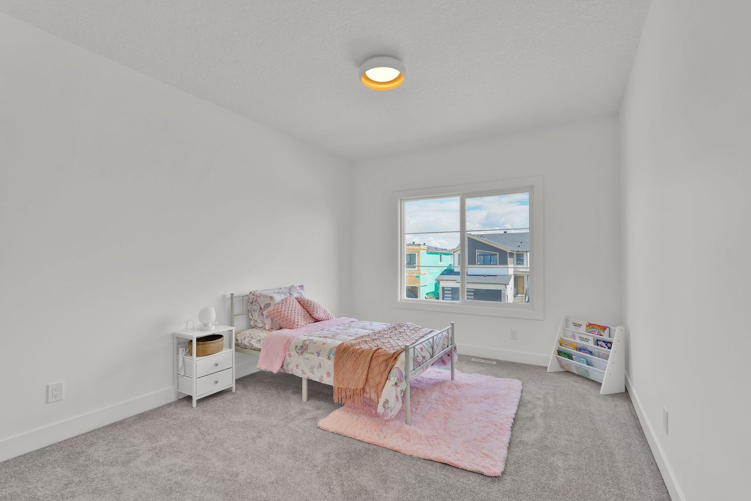 Bright kids bedroom with pink carpet, metal bed frame, white furniture, and large window.