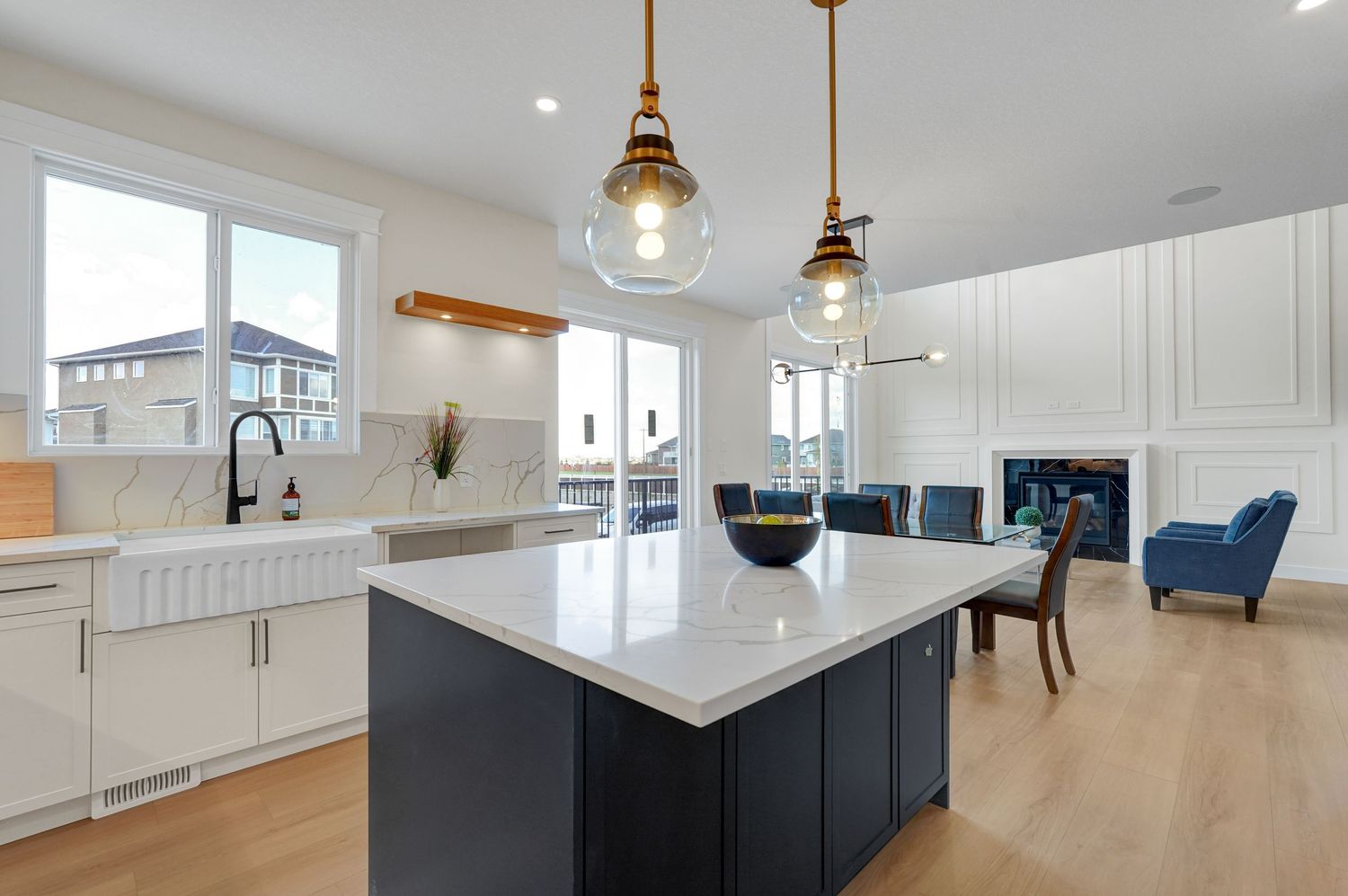 Modern white kitchen with navy island, quartz counters, pendant lights, and farmhouse sink.