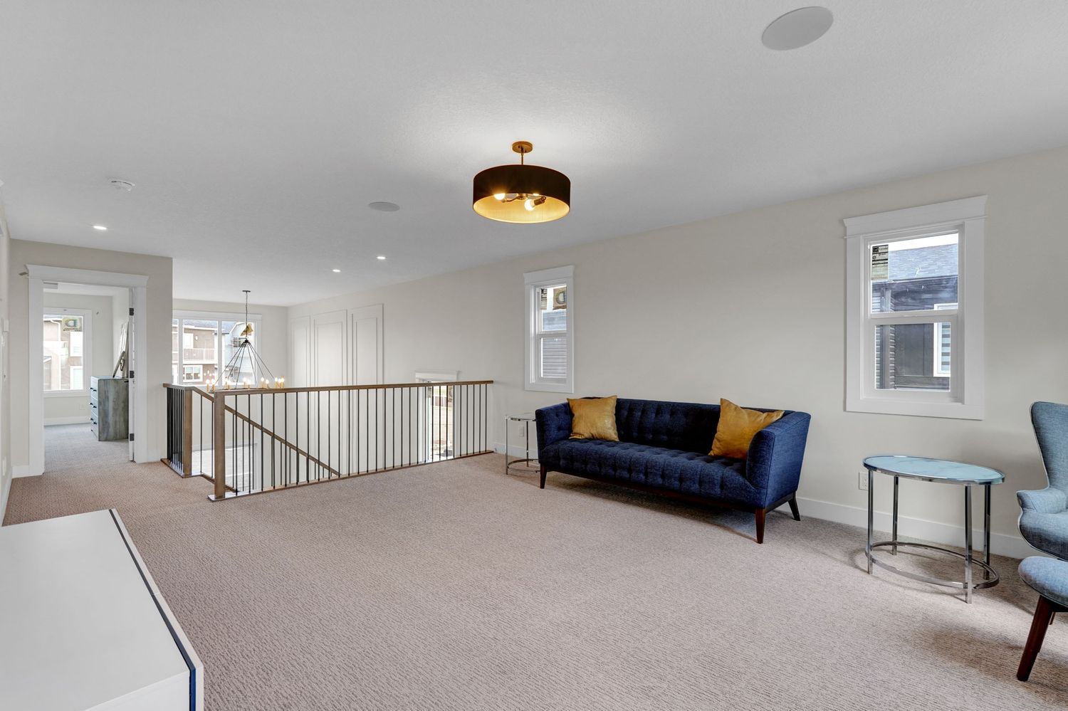 Spacious carpeted bonus room with blue sofa, open staircase railing, and large windows.