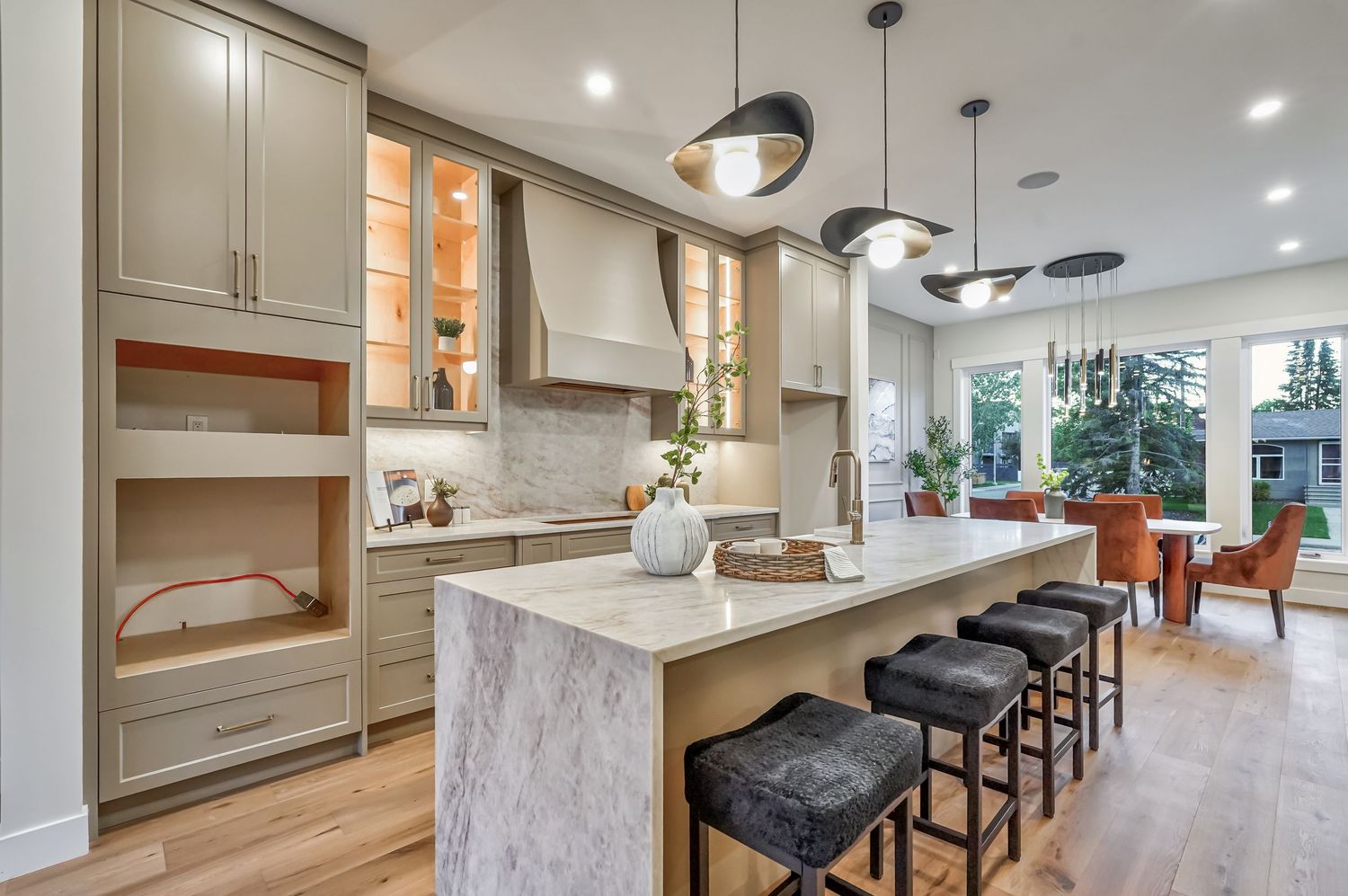 Modern kitchen with gray cabinetry, marble island, black barstools, pendant lights, and hardwood floors.