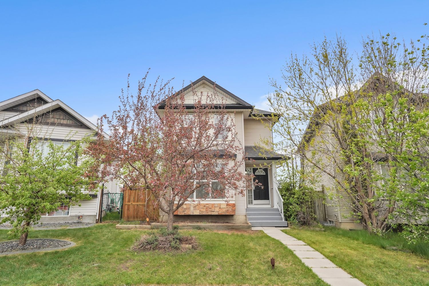 Two-story residential home featuring a pink flowering tree, wood fence, and lush green grass in spring.