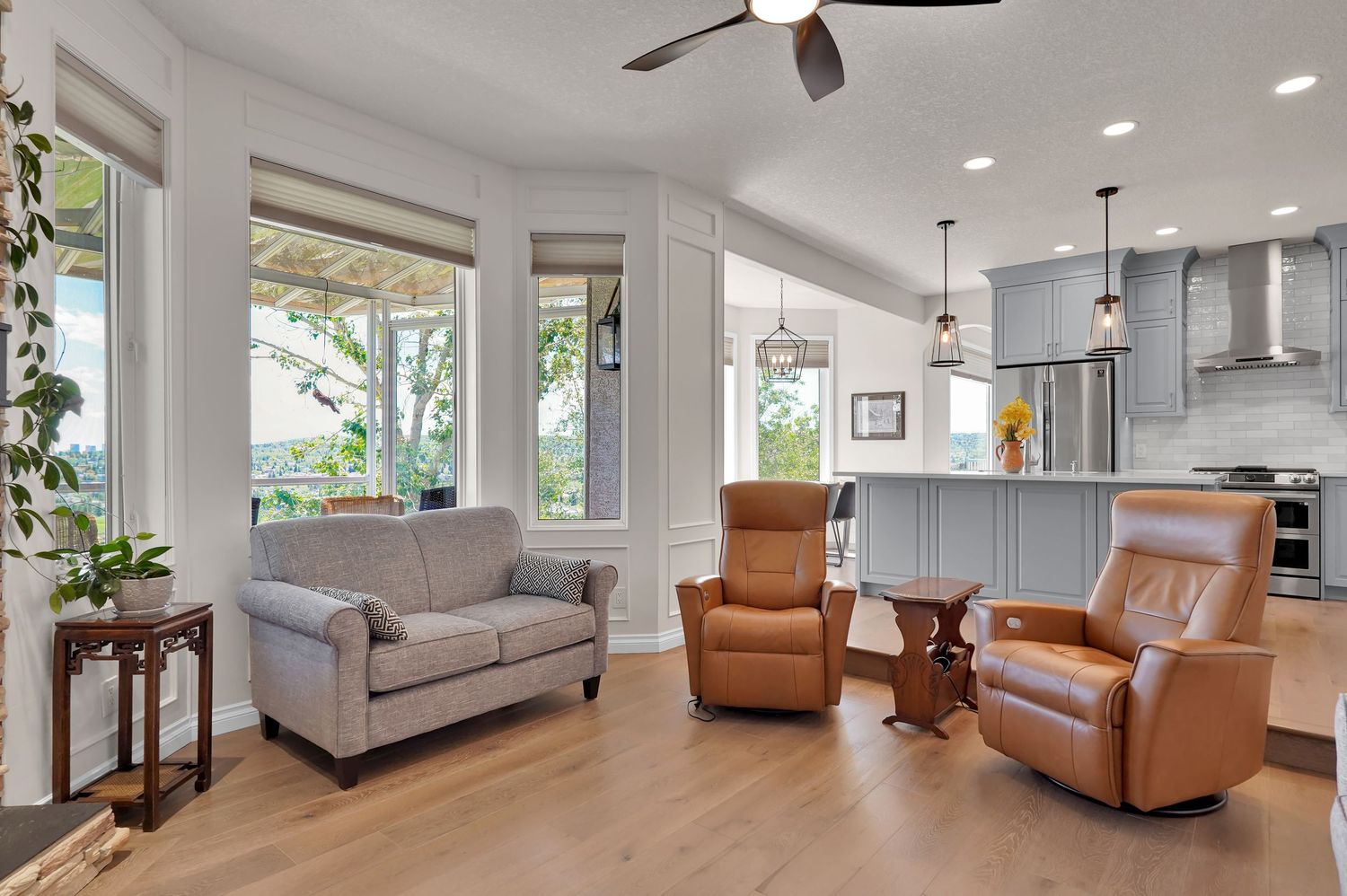 Open-concept living room with gray sofa, leather recliners, hardwood floors, and modern kitchen with pendant lights.