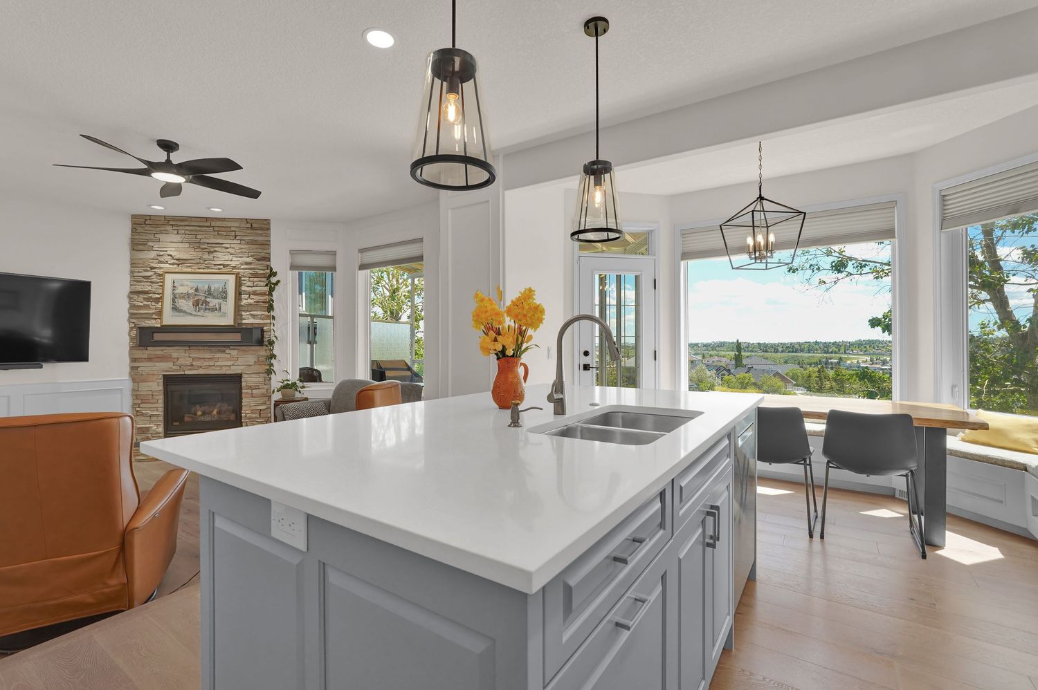 Modern kitchen island with white quartz countertop, gray cabinets, pendant lights, and scenic views through large windows.