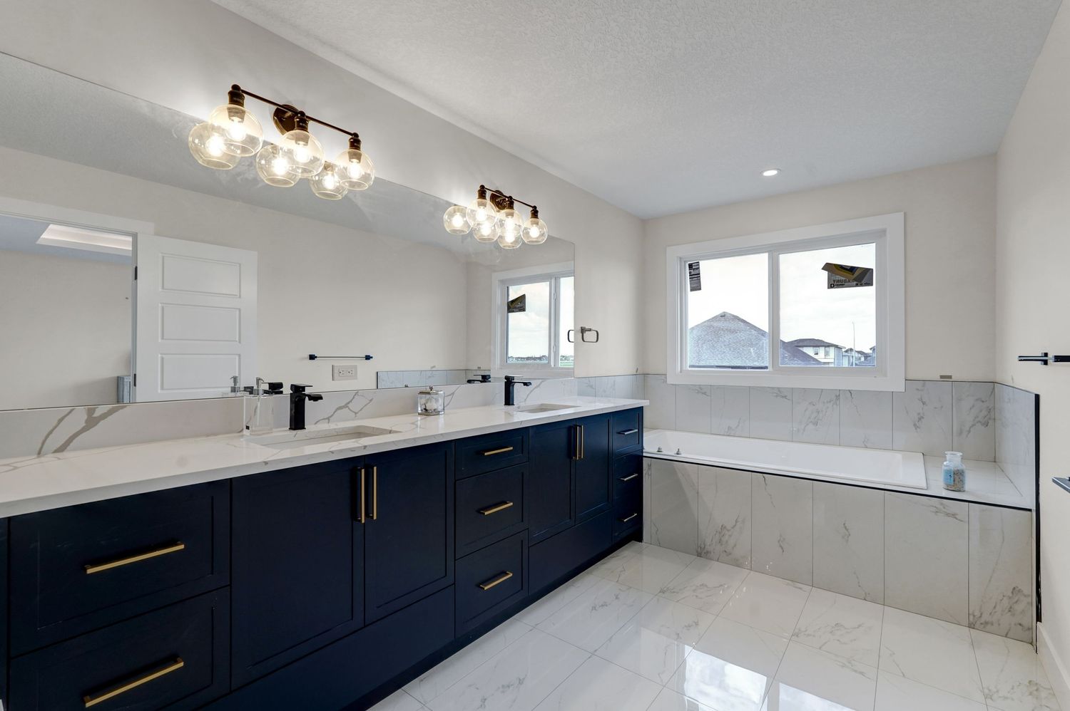 Elegant master bathroom featuring navy blue double vanity, gold accents, marble countertop, and soaking tub.