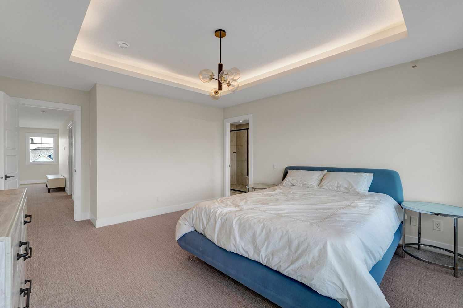 Spacious master bedroom with tray ceiling, chandelier, blue upholstered bed, and neutral carpet.