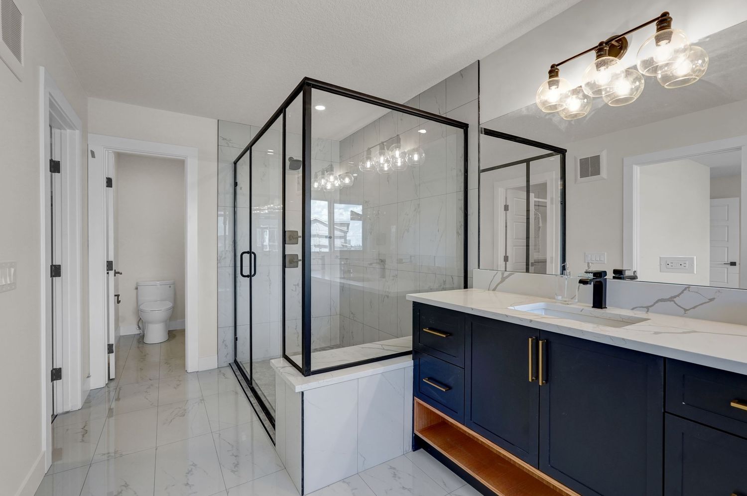 Stylish bathroom with navy blue vanity, black-framed glass shower, marble floors, and gold light fixtures.