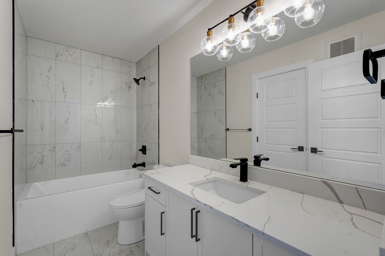 Clean white bathroom with marble tile surround tub, dual sink vanity, black fixtures, and large mirror.