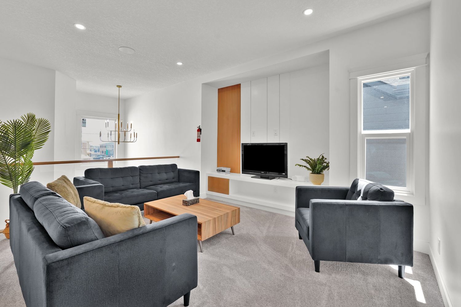 Modern living room with gray sofas, wooden coffee table, wall-mounted TV, and bright white walls with recessed lighting.