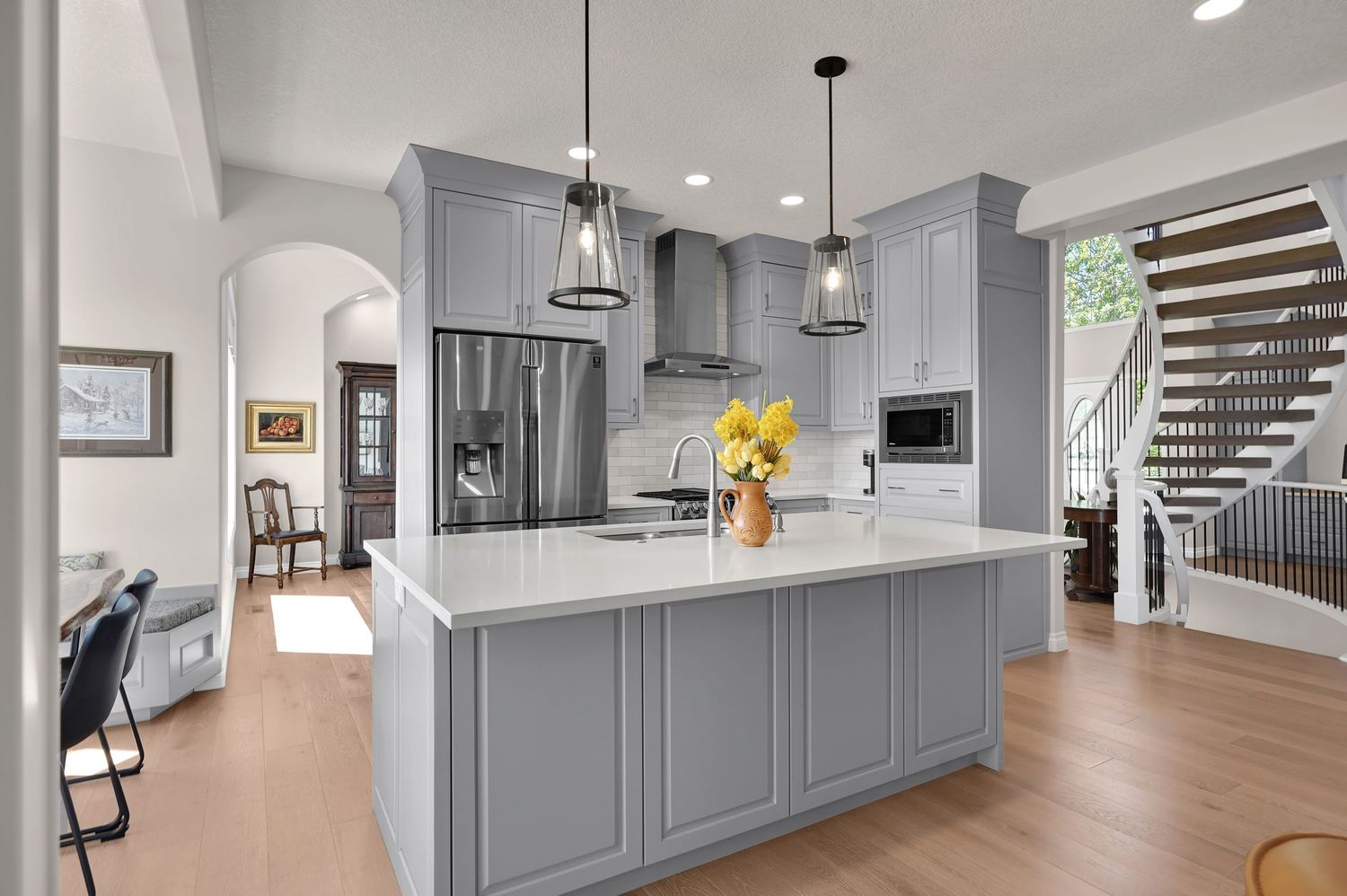 Modern gray kitchen with white quartz island, pendant lights, stainless steel appliances, and hardwood floors.