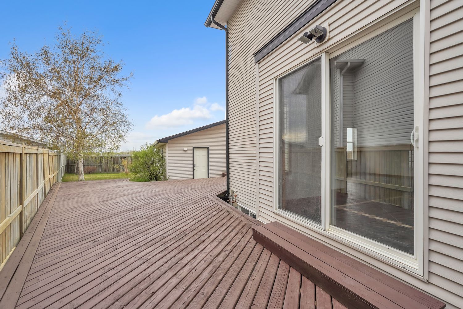 Large wood deck with sliding glass door access and detached garage visible in backyard.
