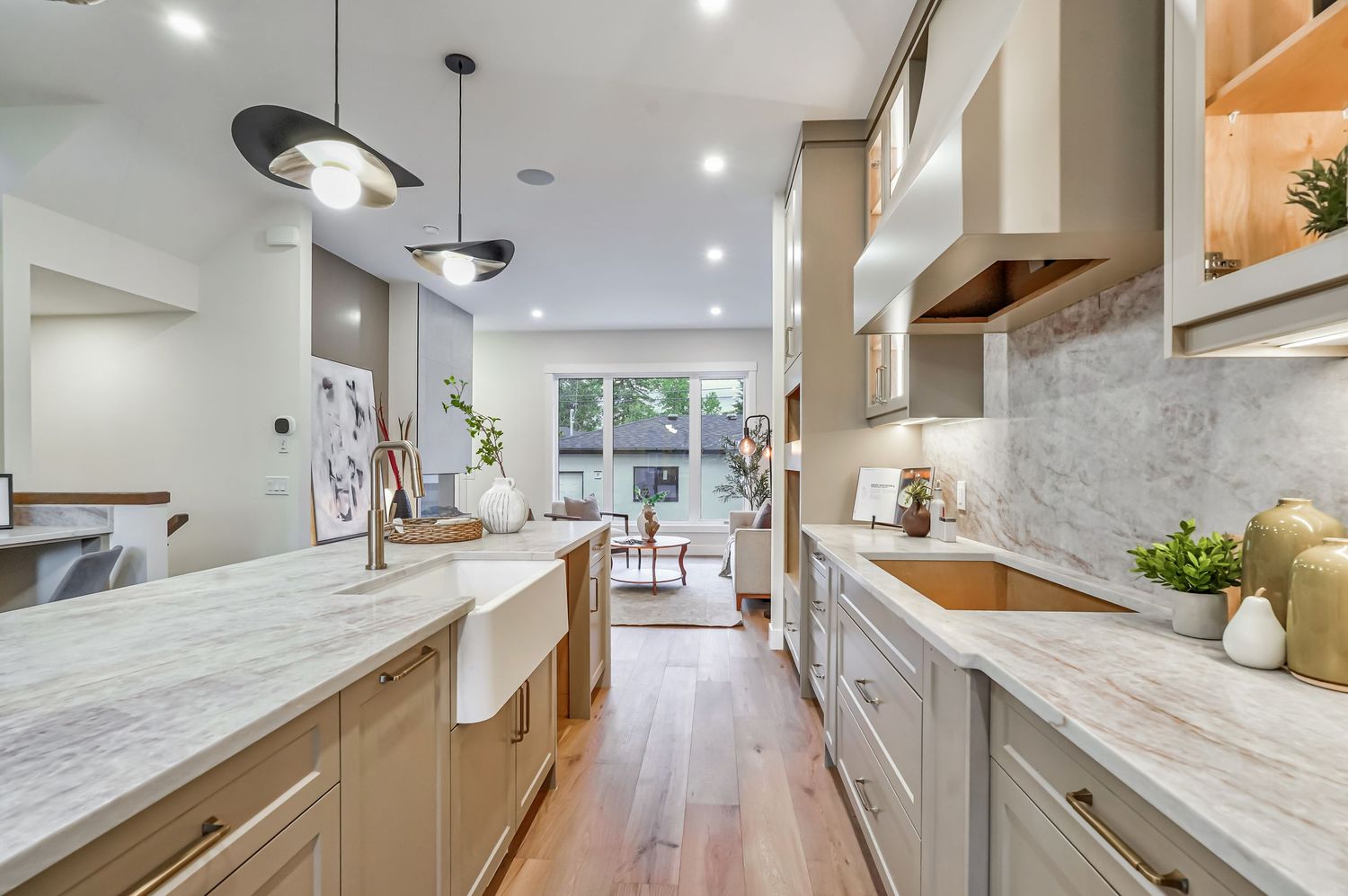 Modern kitchen with marble countertops, farmhouse sink, pendant lights, and light wood floors.
