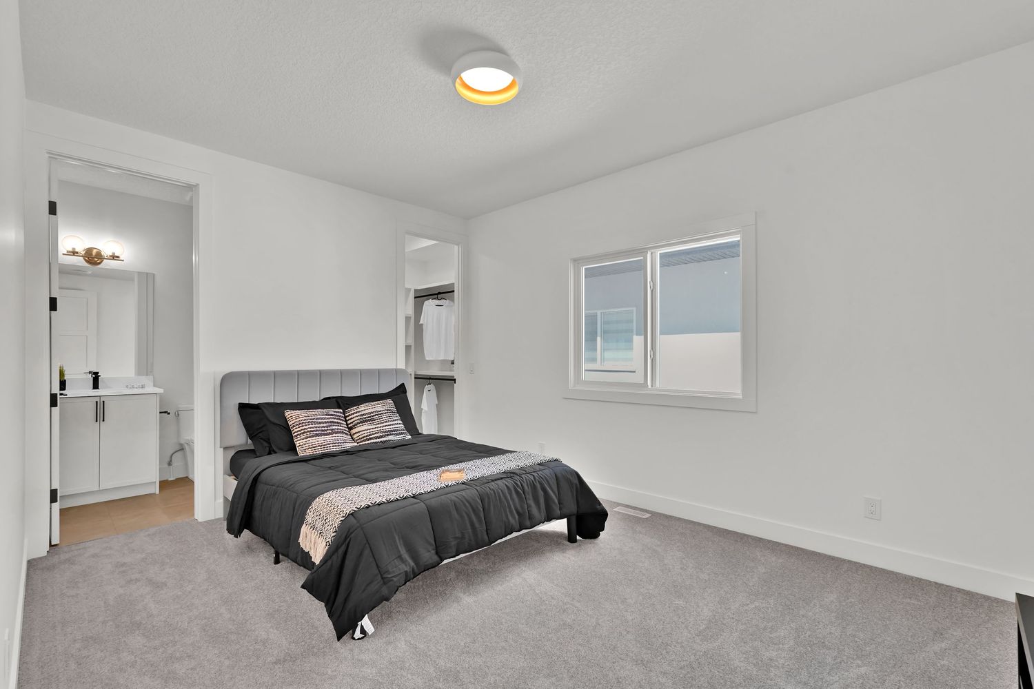 Bright primary bedroom with gray carpet, large window, and ensuite bathroom access in a modern home.
