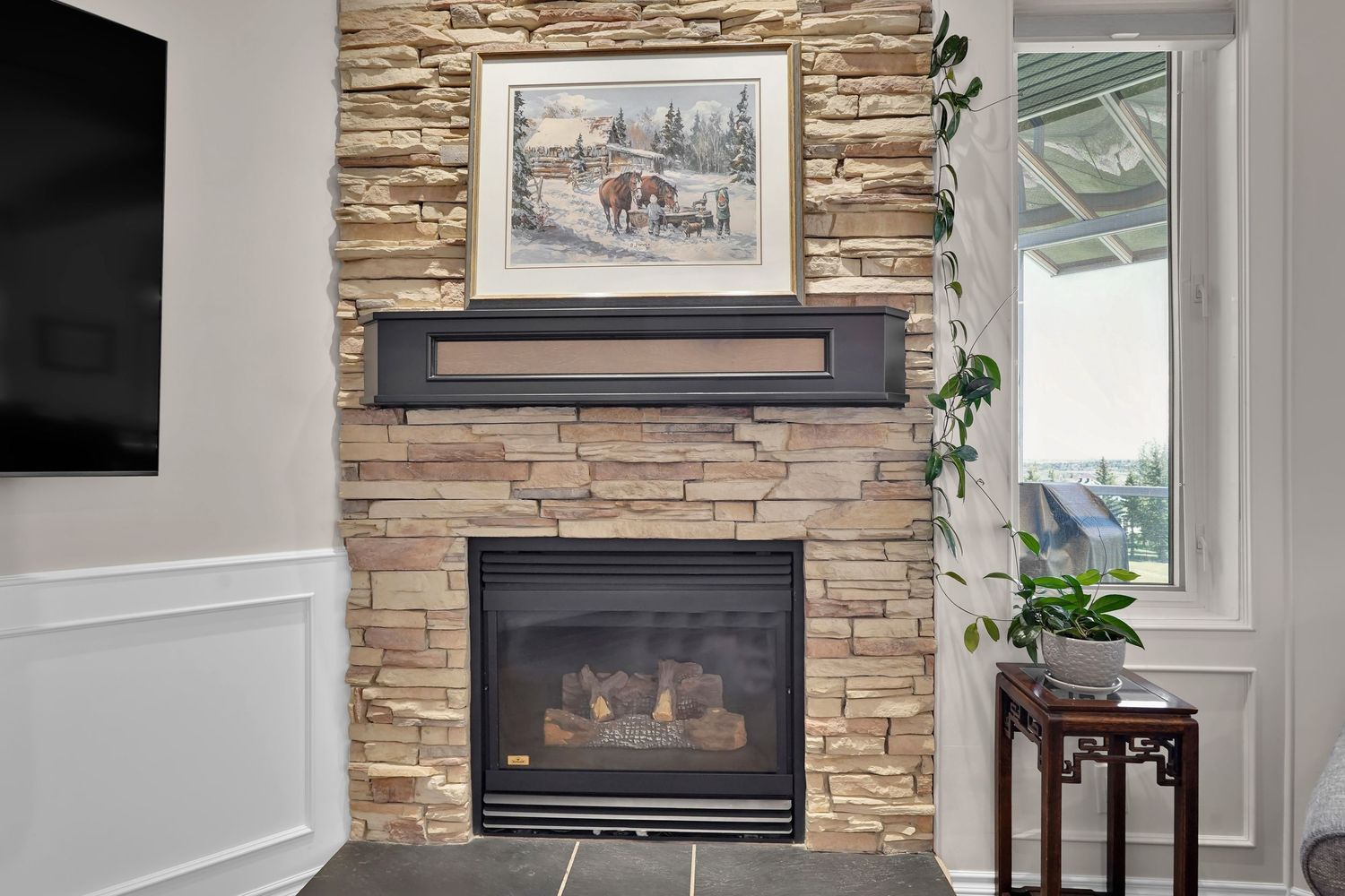 Stone fireplace with wood mantel, framed artwork above, and a small side table in a cozy living room corner.