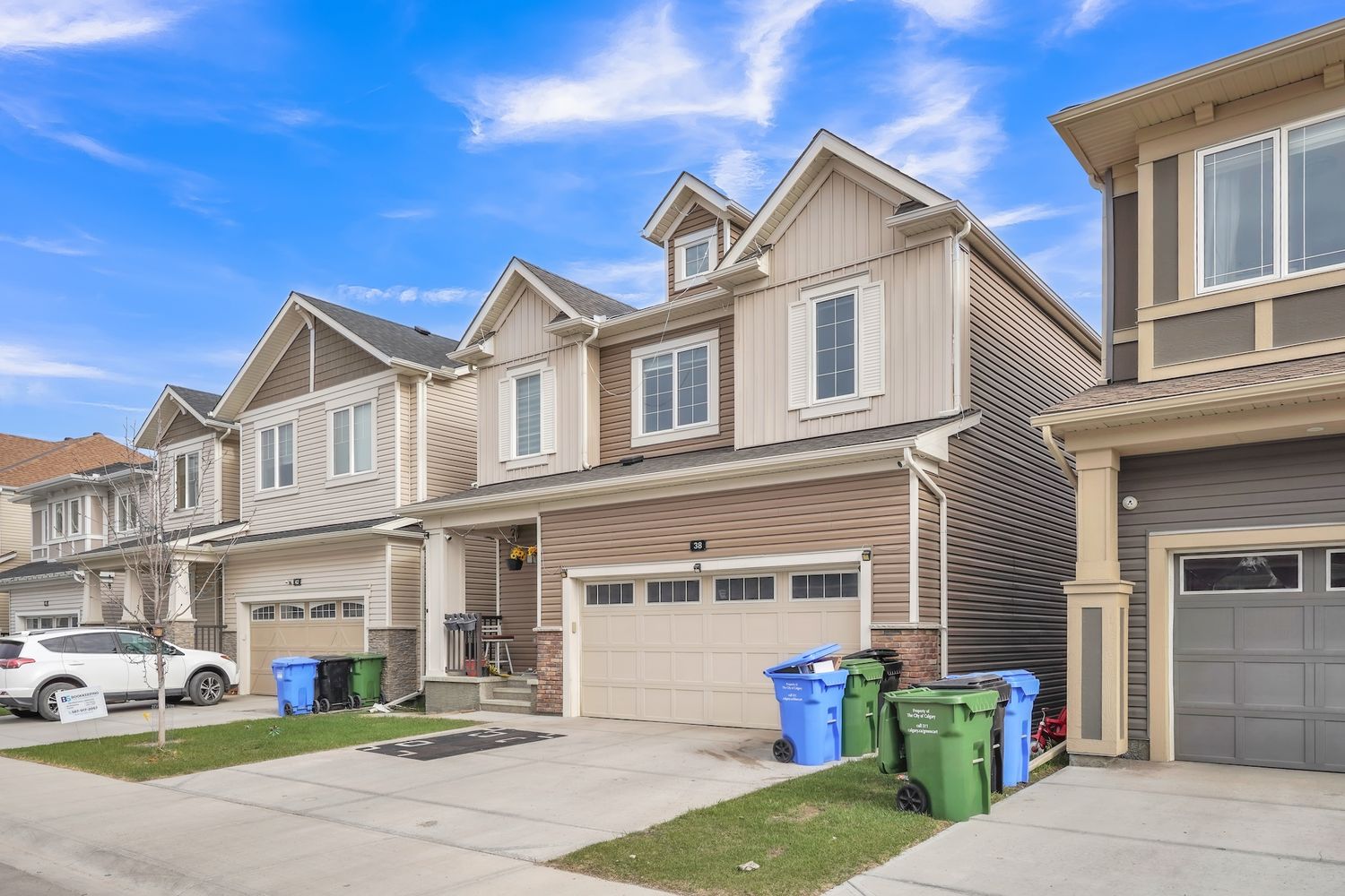 Modern townhouse row with attached garages, neutral siding, and well-maintained front yards under blue sky.