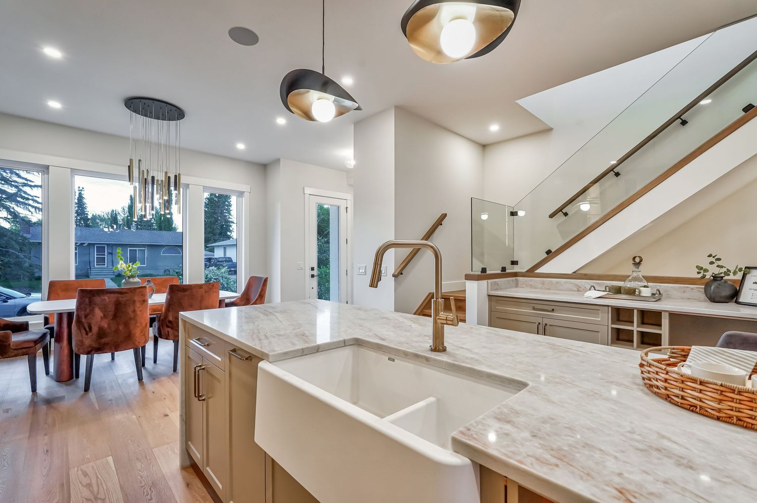 Modern kitchen with marble island, farmhouse sink, gold faucet, pendant lights, and open dining area with hardwood floors.