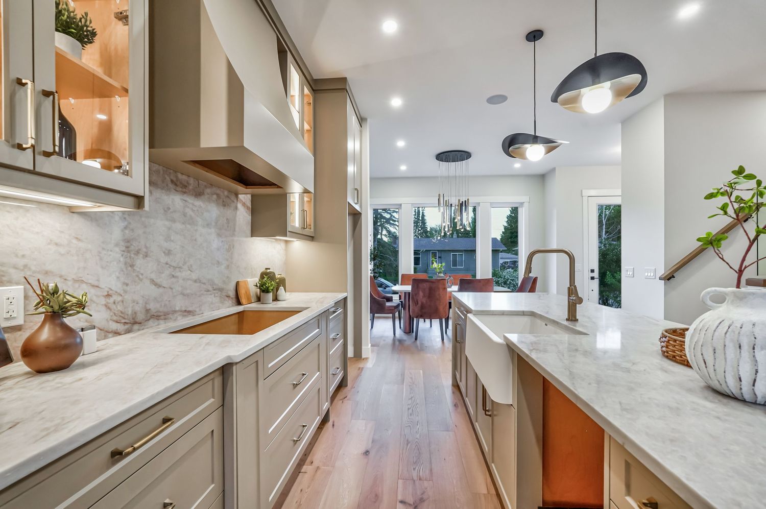 Modern kitchen with marble countertops, gray cabinets, pendant lights, and hardwood floors leading to a bright dining area.
